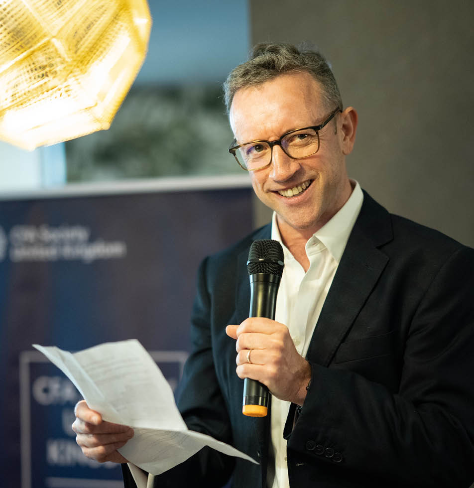 Man smiling at camera with a microphone and a speech in hand