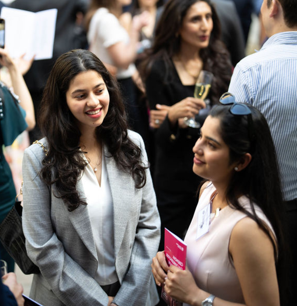 Two women standing outside, with smiles on their face. One is holding a event program 